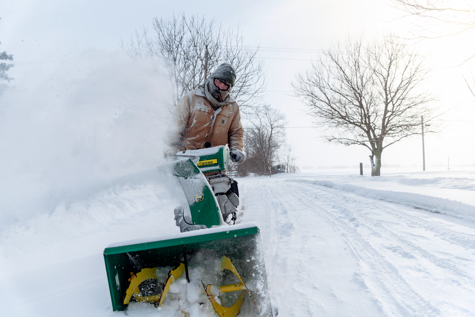 Operator clearing a snowy road with a snow blower