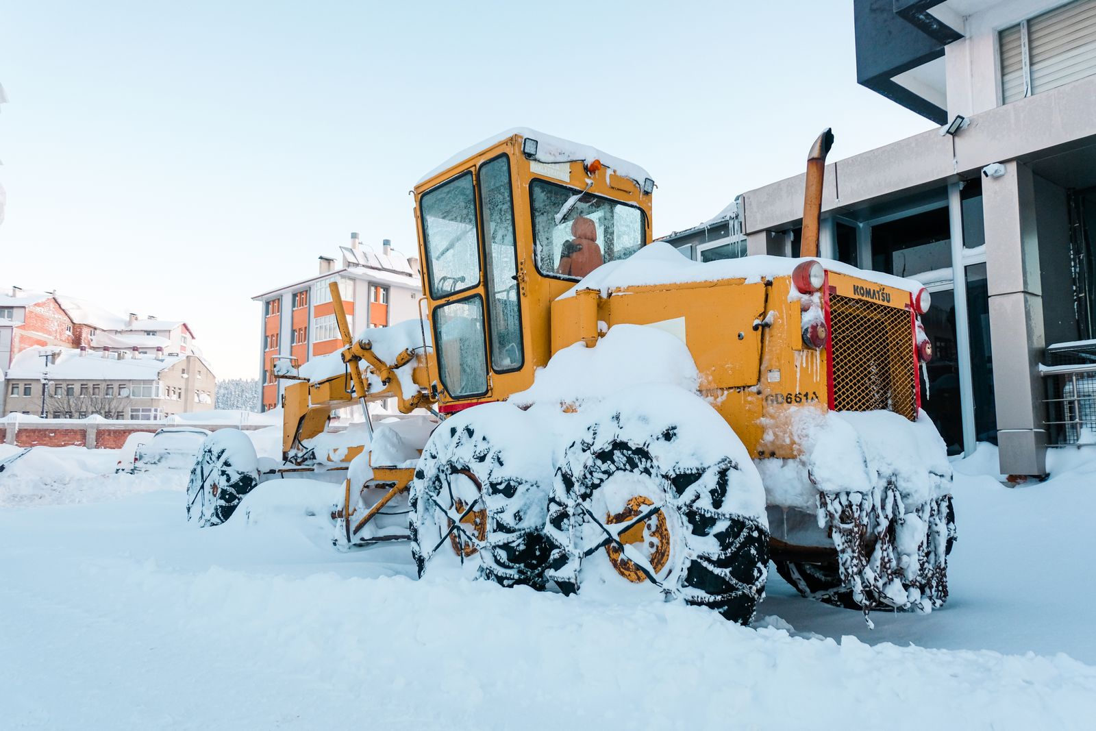 Snow-covered bulldozer parked on a snowy street, ready for snowbank removal