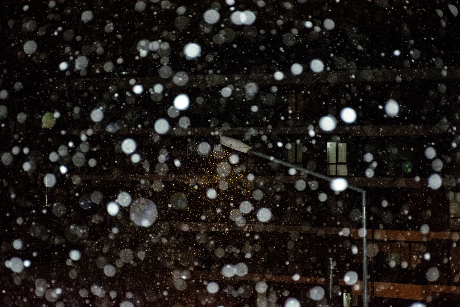 Night snowfall with warm light bokeh on an urban street